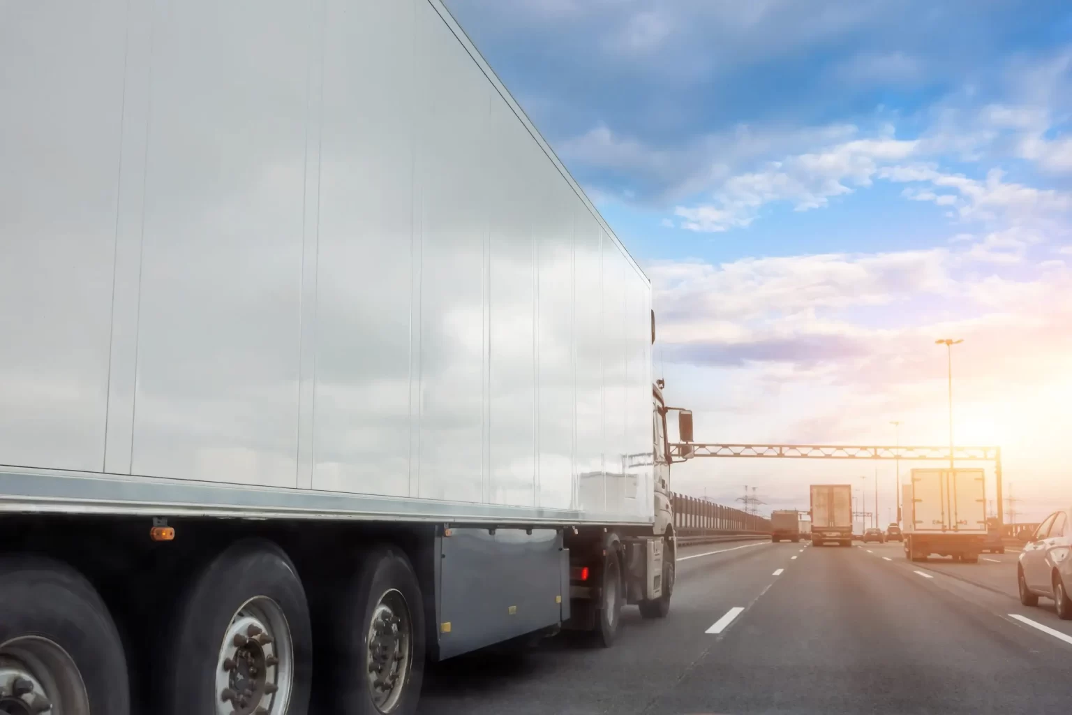Truck with a white trailer drives along the highway in heavy traffic in the evening at sunset